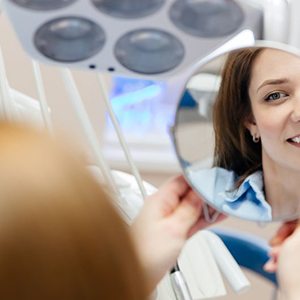 Dental patient’s happy face reflected in hand mirror