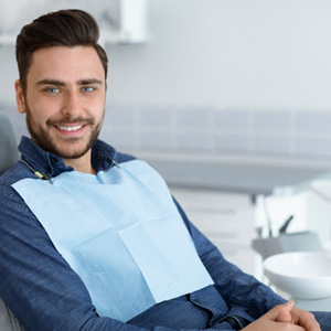 Man in dental chair smiling with hands folded