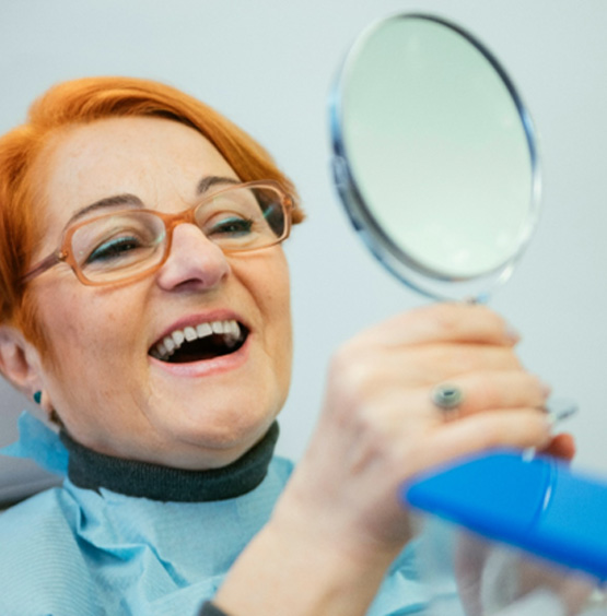 Patient in Falmouth smiling in mirror after preventing dental emergencies